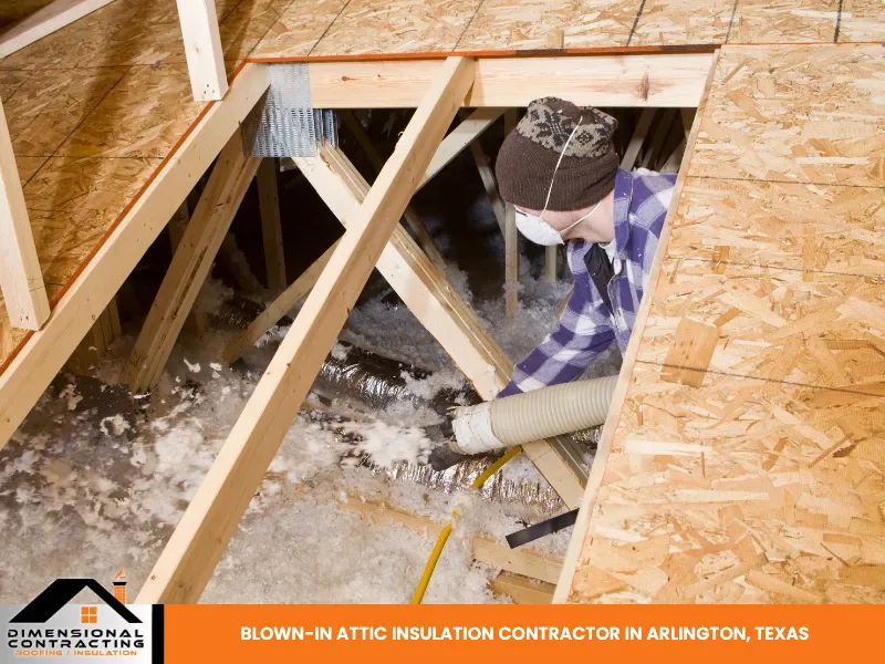 A worker feeding a blown-in insulation hose through a decked opening into an attic.